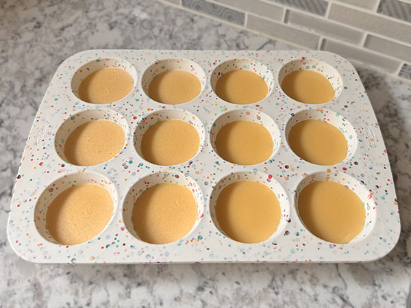 Gummy mixture distributed between silicone muffin pan cups.