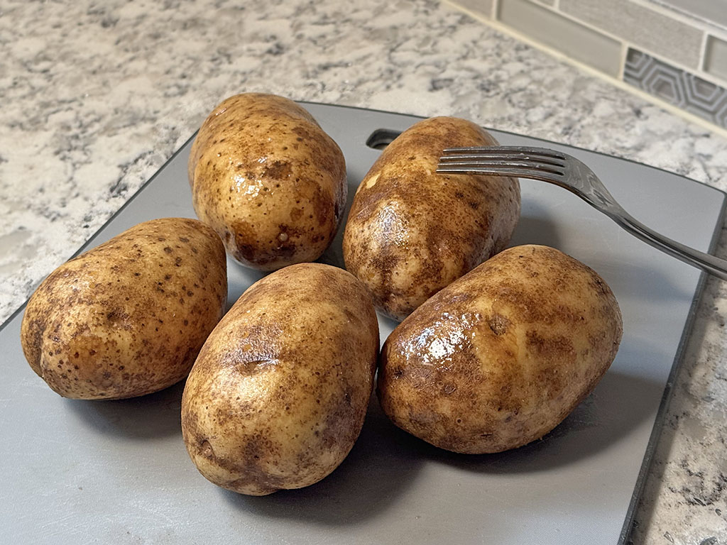 Cleaned raw potatoes, pierced all over with a fork and evenly coated in oil, ready for baking.