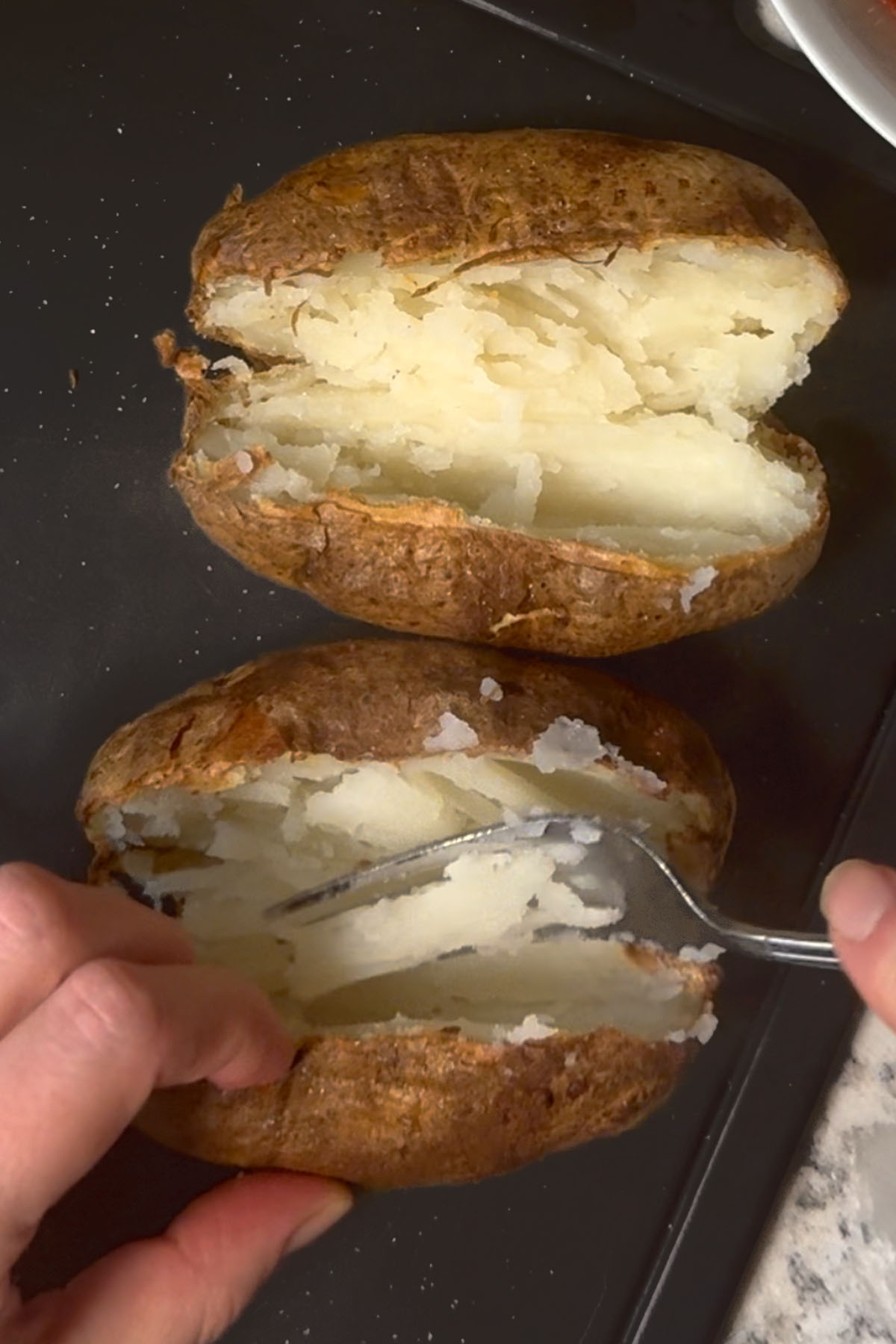 Baked potatoes with a slit, being fluffed inside with a fork.