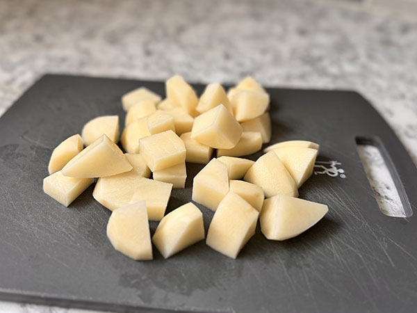 Сырой картофель, нарезанный кубиками, на разделочной доске.