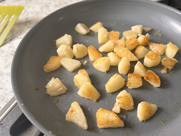 Crispy potato cubes in a skillet.