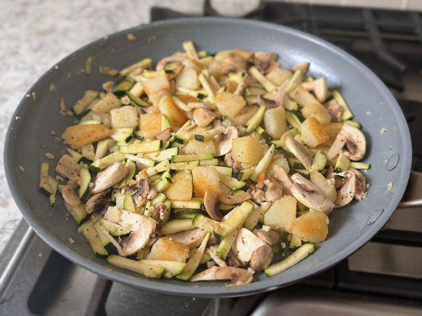 Breakfast potatoes, zucchini, mushrooms and garlic cooking in a skillet.