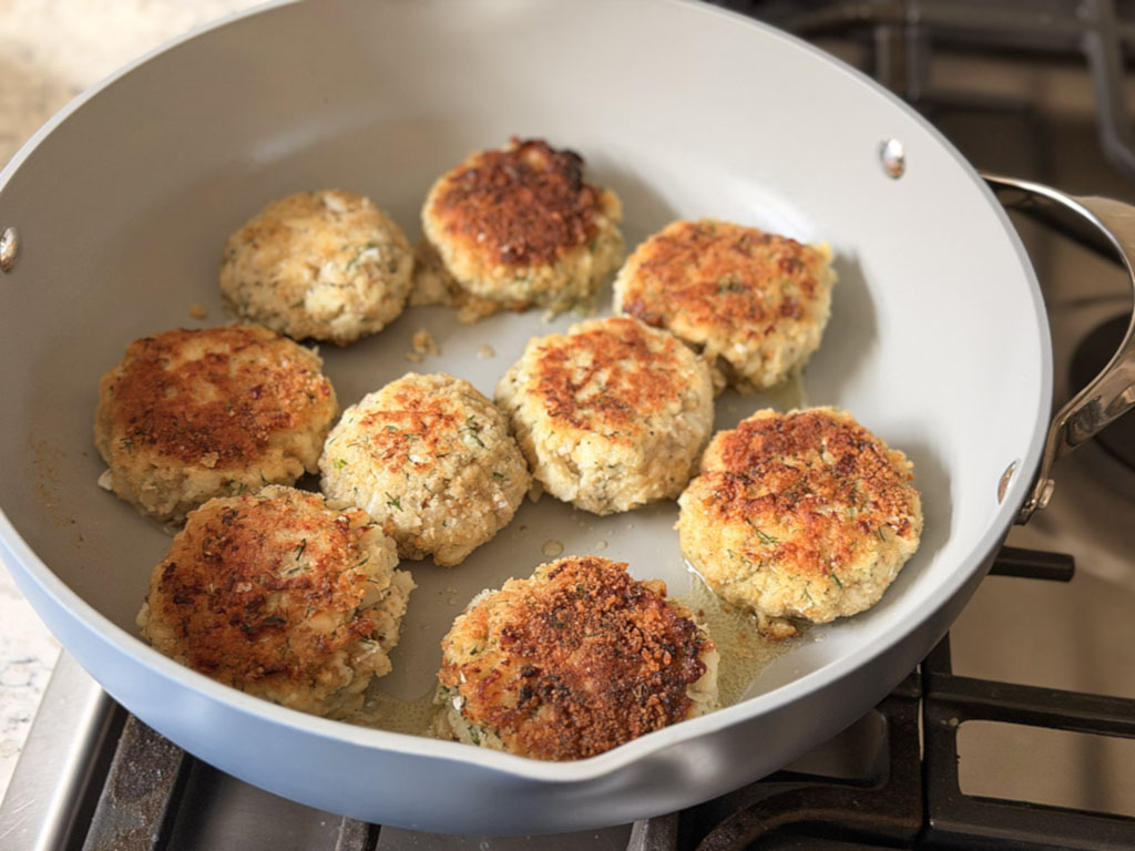 Cod fish cakes flipped in a skillet and cooking until golden and cooked through.