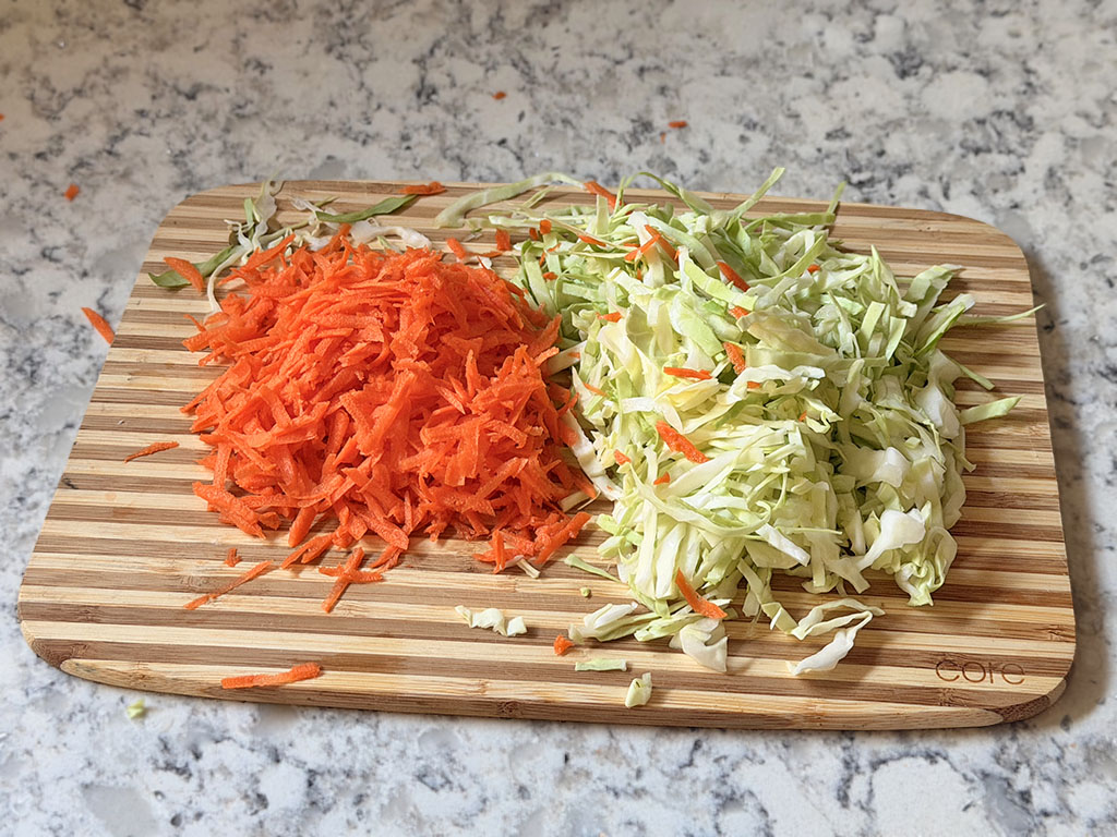 Thinly sliced cabbage and grated carrot on a cutting board.