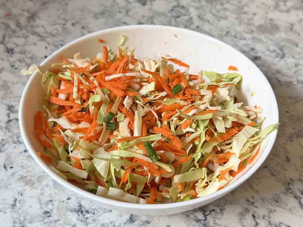 Shredded cabbage, grated carrot and chopped green onions mixed in a bowl.