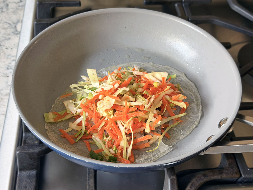 Rice paper topped with shrimp and veggies in a skillet.
