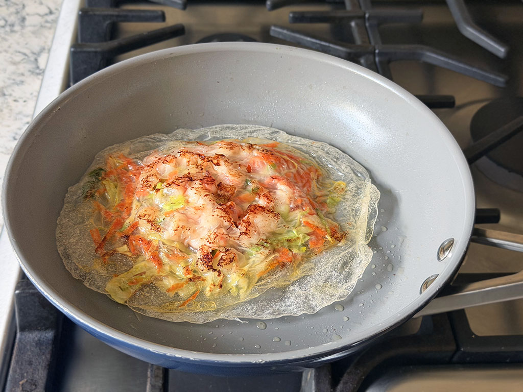 Crispy rice paper pancake frying in a pan on the second side.