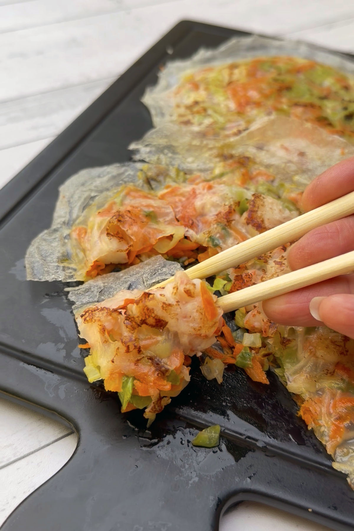 Crispy rice paper shrimp and vegetable pancake cut into serving pieces, with one piece held between chopsticks.