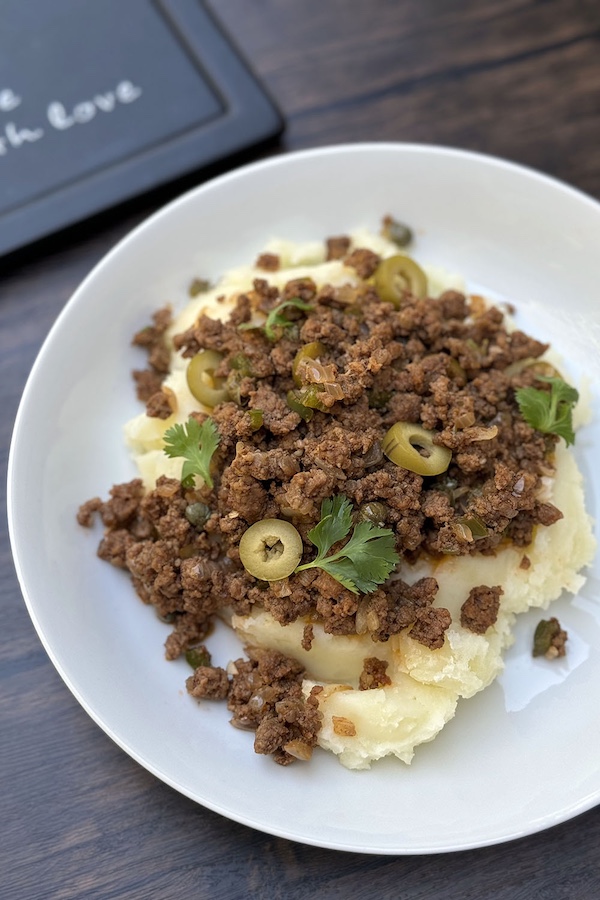 Cuban ground beef and tomato picadillo in a bowl, served over mashed potatoes.