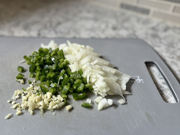 Chopped onion, diced jalapeno and minced garlic on a cutting board.