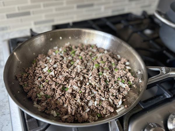 Ground beef with vegetables and spices cooking in a skillet.