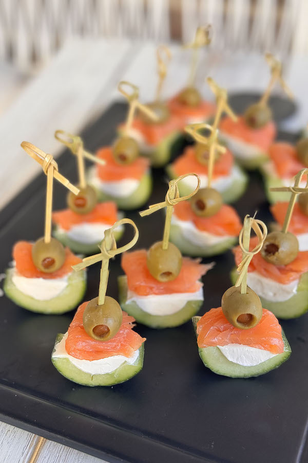 Cream cheese cucumber skewer bites with smoked salmon and manzanilla olives on a serving board.