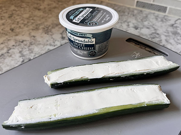 English cucumber halves filled with cream cheese and a cream cheese tub in the background.