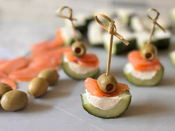 Cucumber bite filled with cream cheese and topped with smoked salmon and pimento stuffed manzanilla olive, threaded on a skewer.