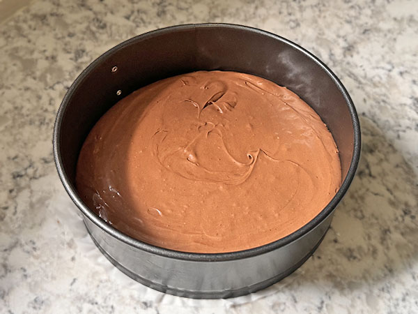 Chocolate cake batter in a parchment lined springform pan.