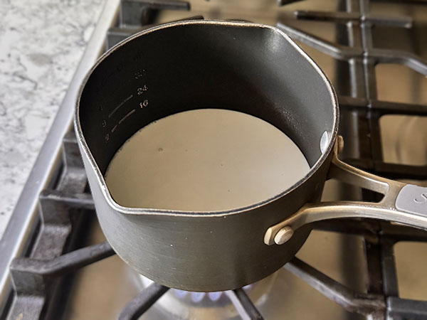 Coconut milk heating in a small saucepan on the stove top.