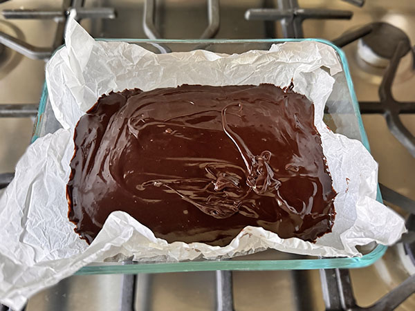 Chocolate truffle mixture in a parchment paper lined glass dish.