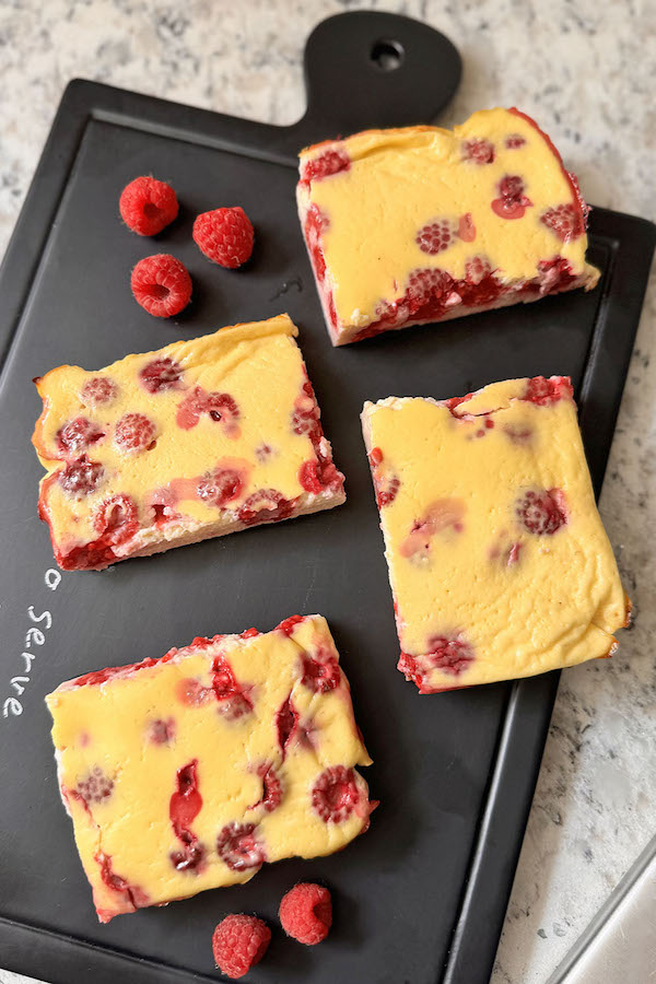 Baked raspberry yogurt cut into square portions on a serving board with fresh raspberries on a side.