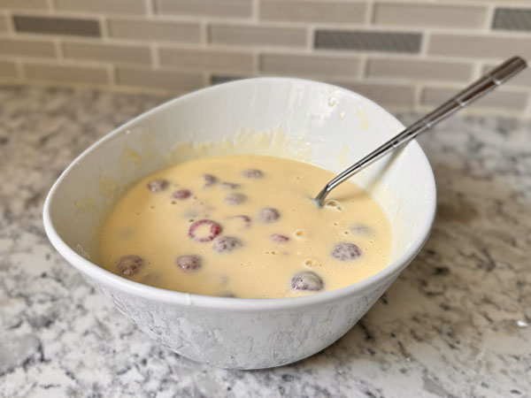 Baked yogurt batter in a bowl with fresh raspberries mixed in.