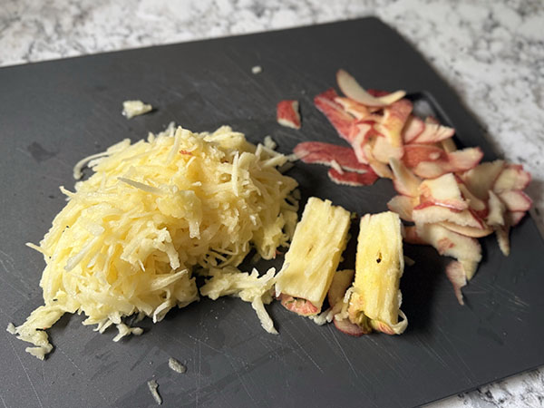 Grated apples on a cutting board, with apple peels and cores on the side.