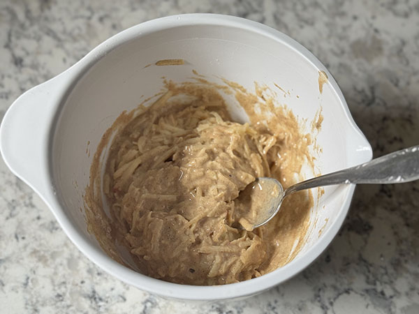 Grated apples mixed in pancakes batter in a bowl.