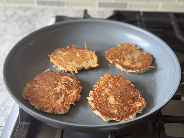 Golden brown apple cinnamon pancakes cooking in a skillet on the second side.