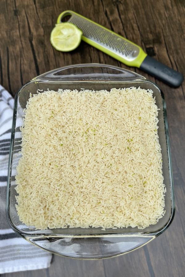 Baked lime rice in a glass dish with a half of lime and zester on the background.