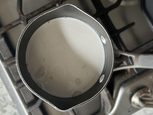 Mixture of coconut milk, water, maple syrup and salt in a pot on stovetop.