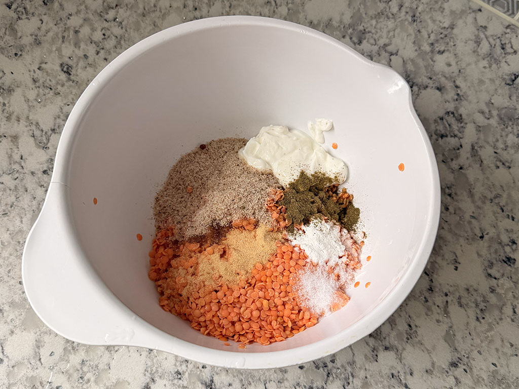 Lentils in a bowl with yogurt, oil, psyllium husks, and seasonings added.