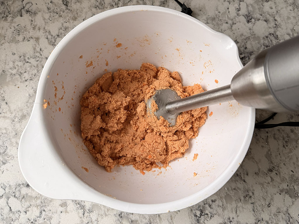 Immersion blender mixing lentil mixture into a thick, smooth dough.
