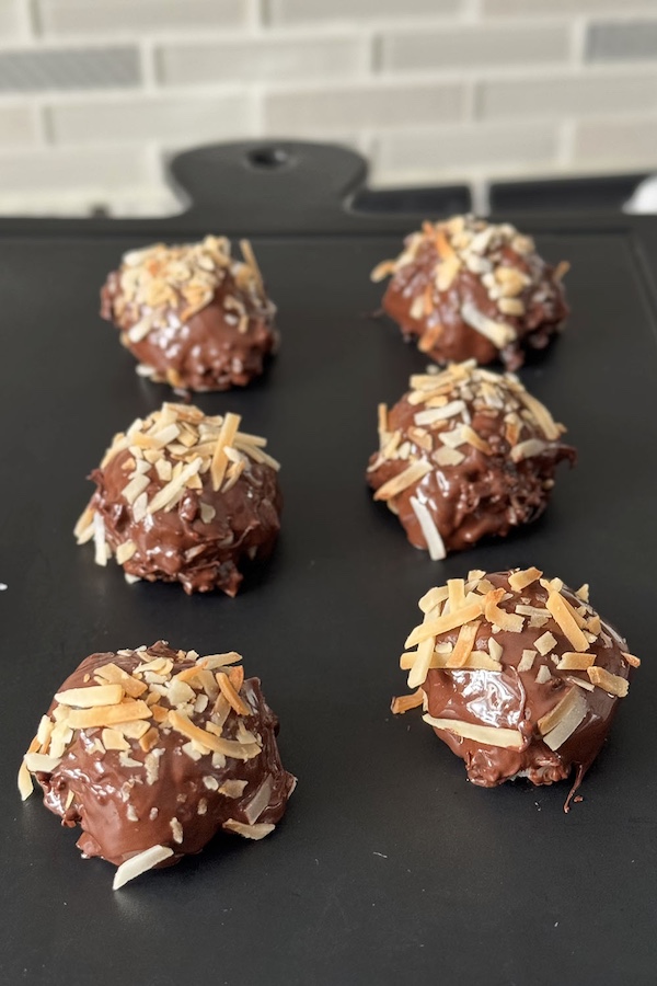 Double chocolate coconut bites topped with toasted coconut, on a serving board.