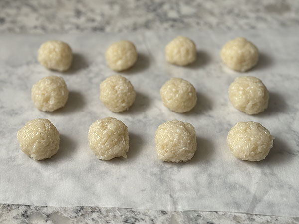 Hand formed coconut balls on parchment lined countertop.