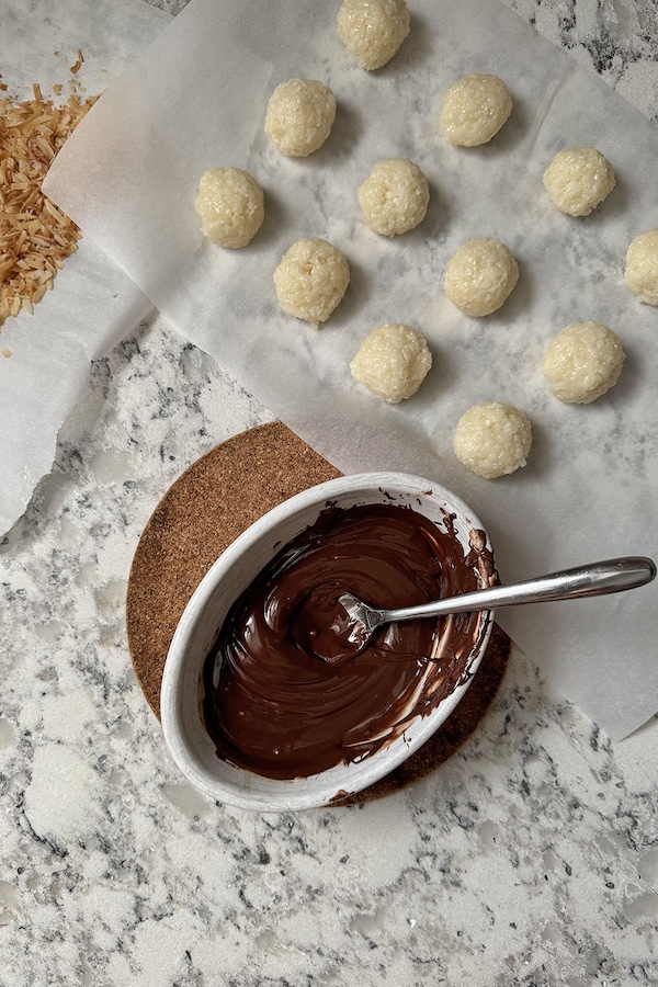 Working station for chocolate coconut balls, includes toasted coconut, melted chocolate and coconut bites.