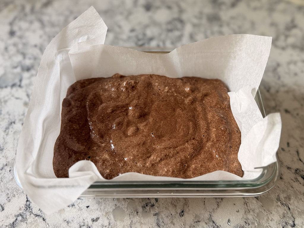 Chocolate banana batter poured into a parchment-lined baking dish and spread evenly.