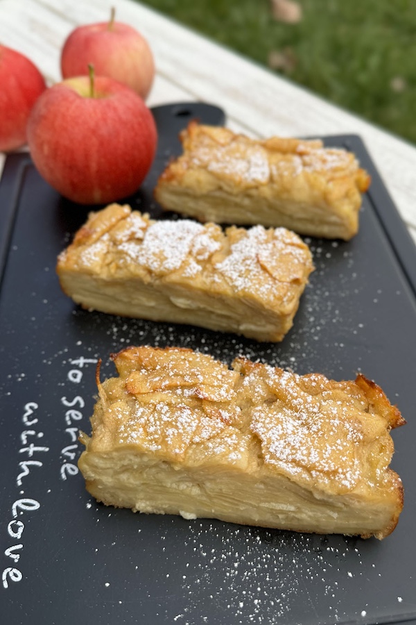 Apple cake slices topped with powdered sugar on a serving board.