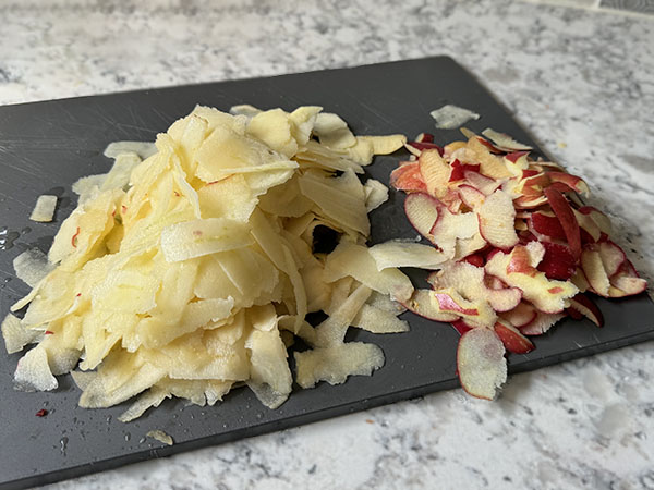 Apples thinly sliced using a vegetable peeler on a cutting board.