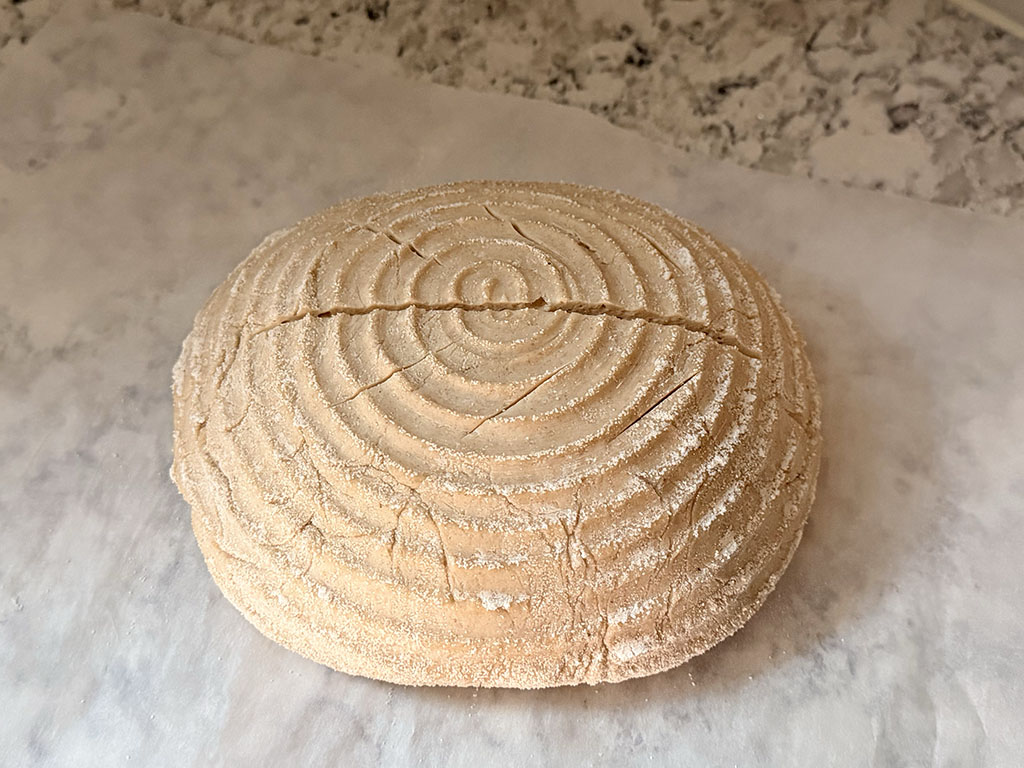 Dough turned onto parchment paper and scored with a deep center slash and small angled cuts along each side, ready for baking.