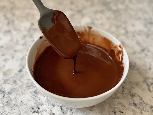 Melted chocolate and ghee mixture in a bowl with a spatula dripping chocolate.