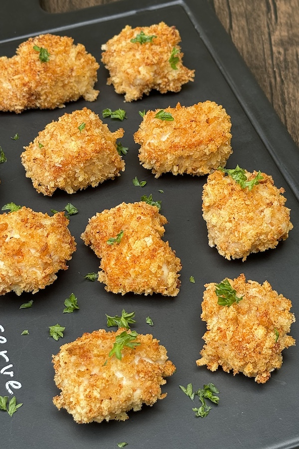 Oven baked chicken nuggets with panko crust, topped with chopped parsley, on a serving board.