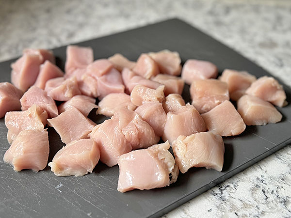 Chicken breasts cut into bite-sized pieces on a cutting board.