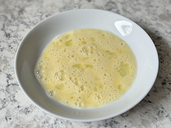 Egg and water mixture whisked together in a bowl.