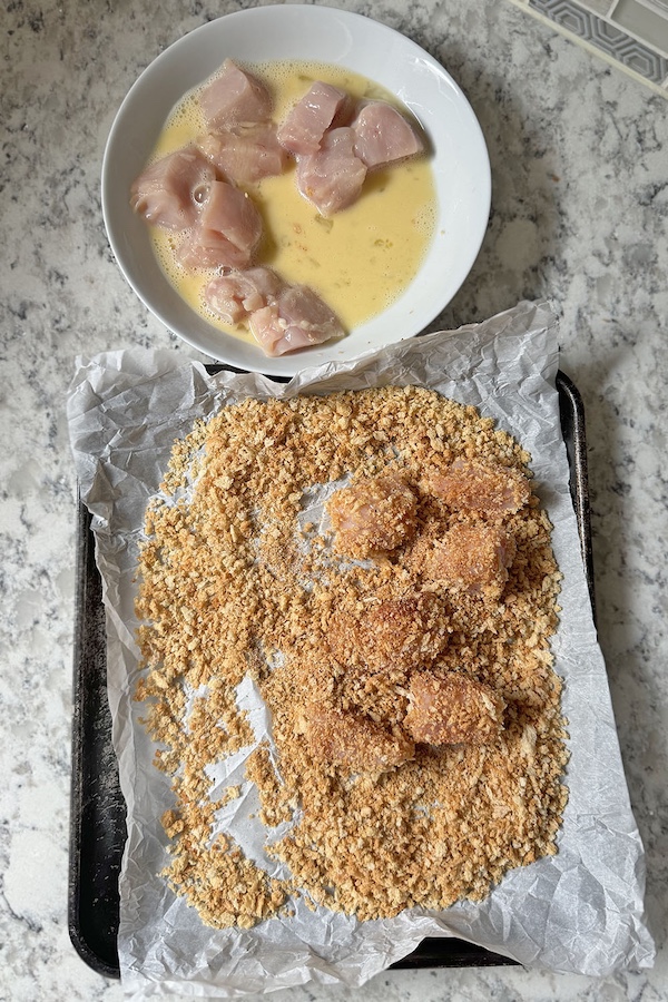 Breading station with chicken pieces dipped in egg mixture and coated in panko breadcrumbs mixture.