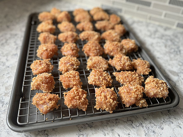 Panko breaded chicken pieces on a wire rack, ready for oven.