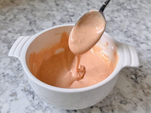 Spicy mayo in a bowl with a spoonful of dripping mayo.