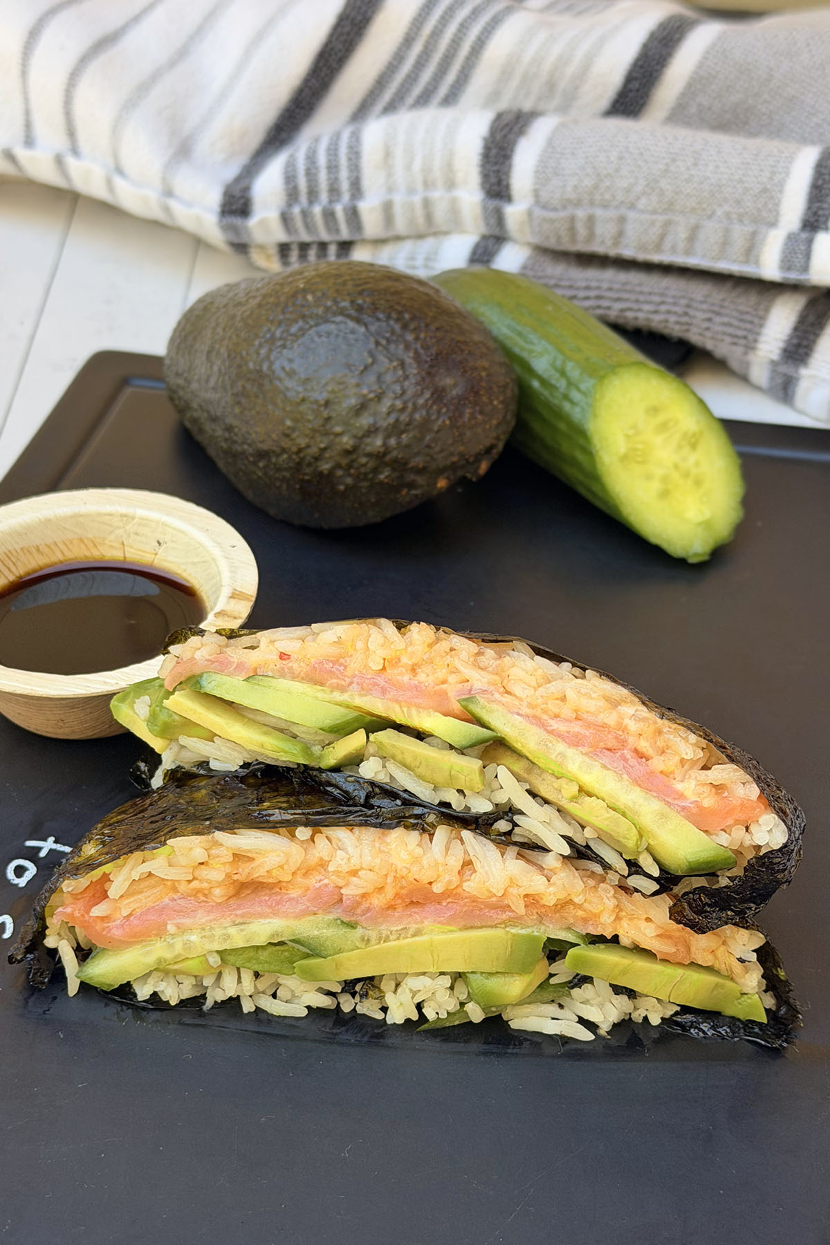 Sushi sandwich halves arranged on a serving board with soy sauce for dipping.