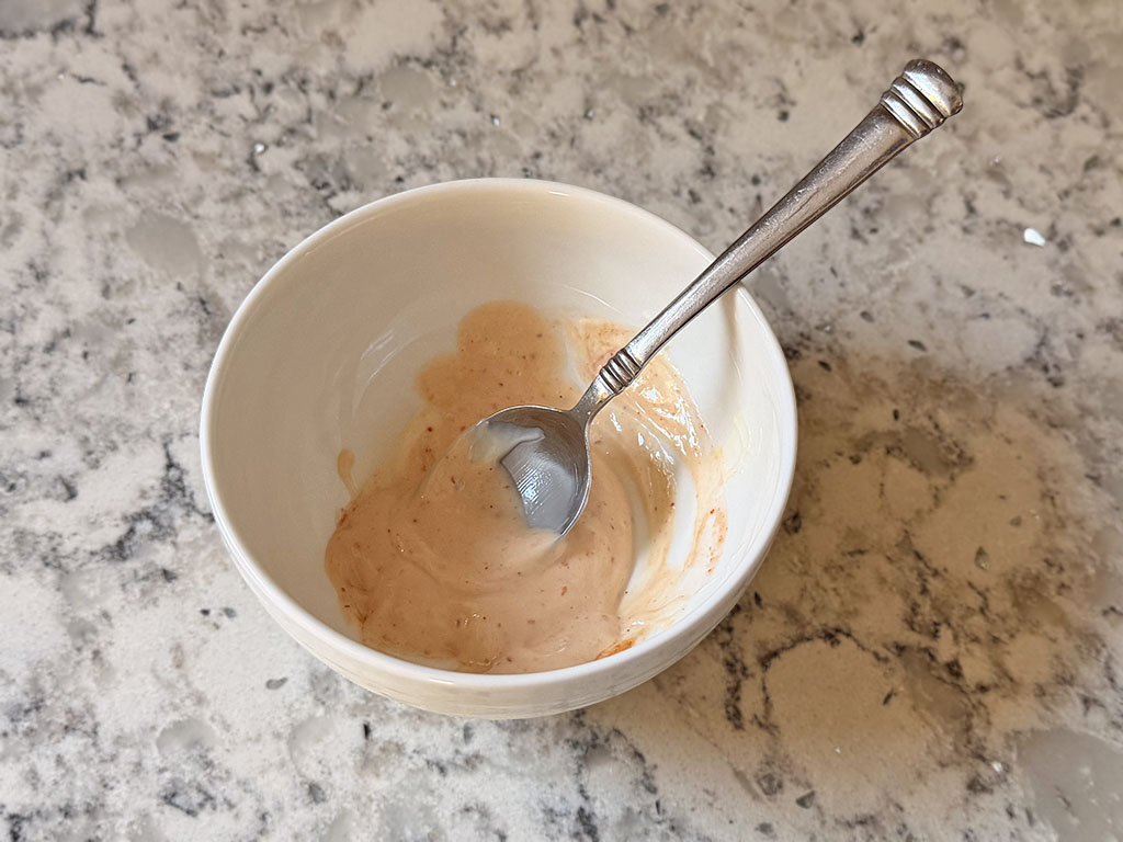 Homemade spicy mayo in a small bowl, freshly mixed with a spoon.