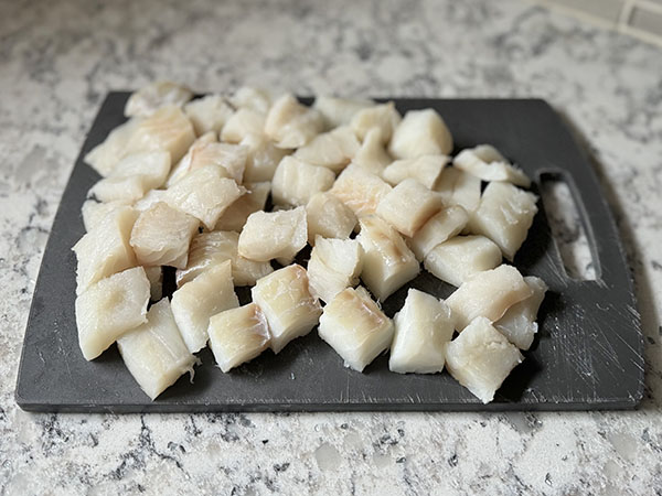 Cod fillets cut into bite-sized pieces on a cutting board.