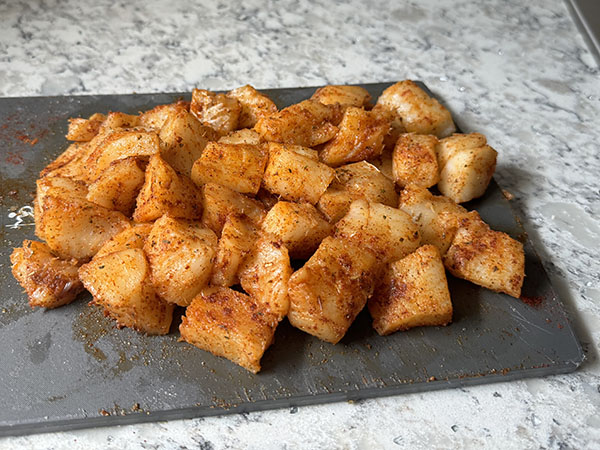 Cod pieces tossed with seasonings on a cutting board.