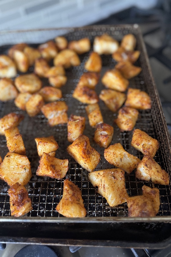 Baked seasoned cod pieces in a rack of the baking sheet, straight from the oven.