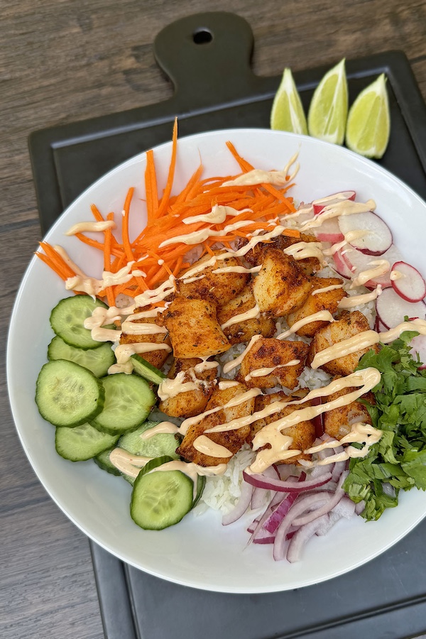 Spiced cod and lime rice bowl with veggies, garnished with lime wedges on a serving board.